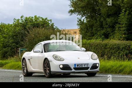 Woburn, Beds, UK - 19 agosto 2023:2010 auto Porsche Cayman bianca che viaggia su una strada di campagna inglese. Foto Stock