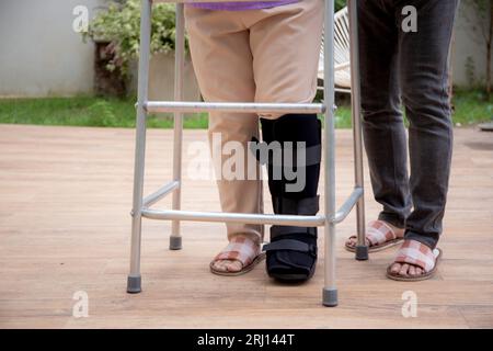 Closeup leg senior man aiuta e sostiene le donne anziane mentre cammina con il camminatore per la riabilitazione e la terapia insieme in giardino a casa, senior c Foto Stock