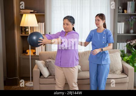 Infermiere asiatica donna o infermiera che forma donna anziana sollevando palla sportiva con le mani per l'esercizio fisico mentre fisioterapia e riabilitazione, custode o Foto Stock