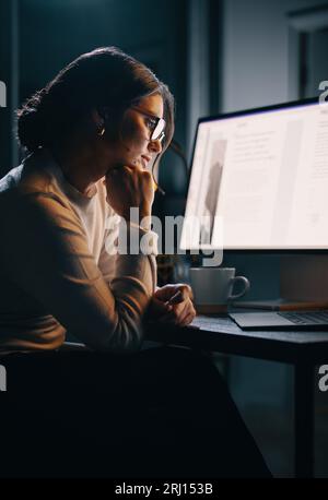 Donna d'affari pensiva lavora sul suo notebook in un ufficio domestico a tarda notte. Concentrata e determinata, pianifica e stratega per il suo progetto, mostrando h Foto Stock