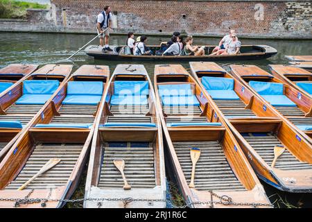 Un punt pieno di turisti passa una fila di punt vuoti legati nell'area Quayside di Cambridge sul fiume Cam nell'agosto 2023. Foto Stock