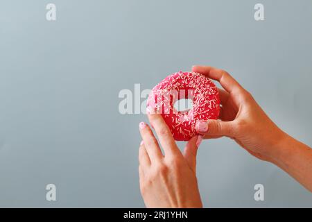 Mano femminile che tiene la ciambella dolce con bellissime unghie rosa Foto Stock