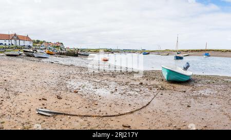 Un panorama multi immagine di una barca a Burnham Overy Staithe con la sua catena e l'ancora che giace sulla costa fangosa del Norfolk settentrionale nell'agosto 2023 Foto Stock