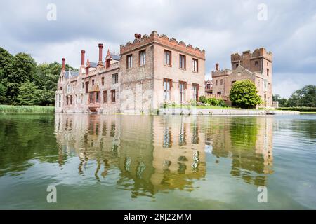 Oxburgh Hall che si riflette nell'acqua del fossato circostante visto in una luminosa giornata estiva a Norfolk nell'agosto 2023. Foto Stock