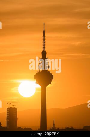 Tramonto con il sole che tocca quasi una torre di comunicazione. Con nuvole nel cielo di Madrid con tonalità arancioni. Foto Stock