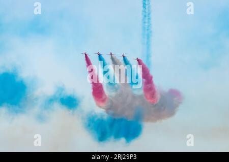 Il famoso team di esposizione della RAF, le frecce rosse, rilasciano fumo rosso, blu e bianco mentre volano verso la spiaggia all'annuale Eastbourne Airbourne, a Foto Stock