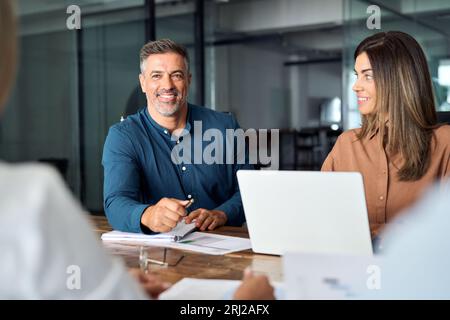 Un vecchio manager latino che discute di strategia con il team aziendale durante una riunione d'ufficio. Foto Stock