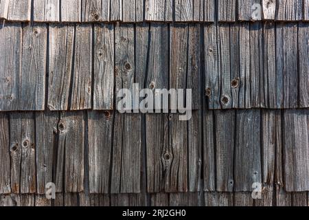 Vecchio cottage di montagna sloveno con facciata in legno piastrellato, piastrelle di legno usurate sul muro esterno come sfondo Foto Stock