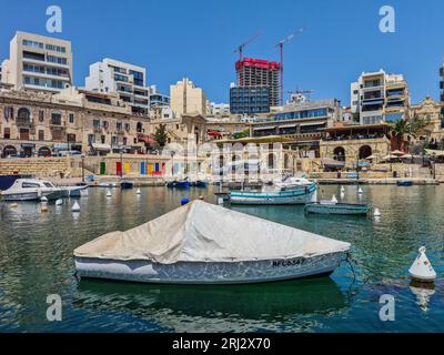 San Giljan (San Giuliano), Malta - 2 agosto 2020: Una barca coperta nella Baia di Spinola circondata da appartamenti e ristoranti. Foto Stock