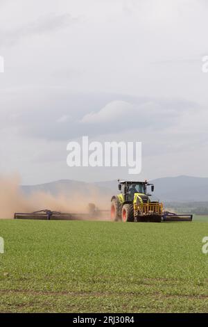 Un trattore Claas Axion 850 che traina un Power Roller dal-Bo 1530 sopra l'orzo primaverile in condizioni di clima secco e crea nuvole di polvere Foto Stock