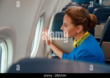 Donna gioiosa stewardess guardando fuori la finestra in aereo Foto Stock