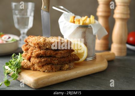 Gustosi schnitzels serviti con coltello e patatine fritte su tavola grigia, primo piano. Spazio per il testo Foto Stock