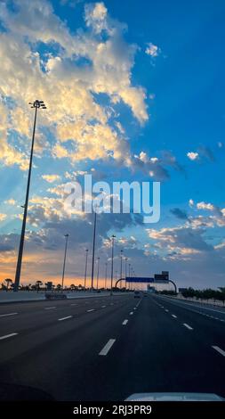 Un vivace cielo arancione e rosa è illuminato dal sole che tramonta, diffondendo una luce calda su un'autostrada tortuosa Foto Stock