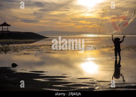 Fisherman indonesiano che lancia una rete con una pagoda sullo sfondo Foto Stock