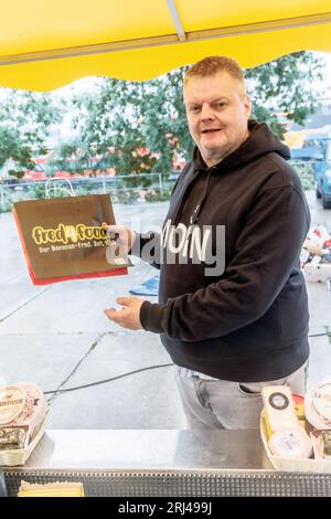 Amburgo, Germania. 23 luglio 2023. Axel Pabst vende formaggio al mercato del pesce di Amburgo. Da più di 25 anni Axel Pabst lavora come market crier per l'azienda Fred4Food, che è diventata nota nel mercato del pesce attraverso il commercio di frutta Bananen-Fred. Nel frattempo, però, non c'è più solo frutta nell'assortimento, ma anche, tra le altre cose, il proprio stand di formaggi. Meglio conosciuto come: Cheese-Fred. (A dpa: "Gridare per Käse-Fred - un venditore di pesce in missione") credito: Markus Scholz/dpa/Alamy Live News Foto Stock