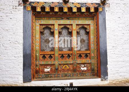 Dettaglio di pannelli decorativi tradizionali scolpiti, dipinti in legno con pesante cornice in legno, incastonati in una parete di pietra bianca a Punakha Dzong, Regno del Bhutan Foto Stock