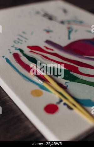 Un pezzo di carta bianco con un dipinto colorato e una selezione di pennelli nelle vicinanze. Foto Stock