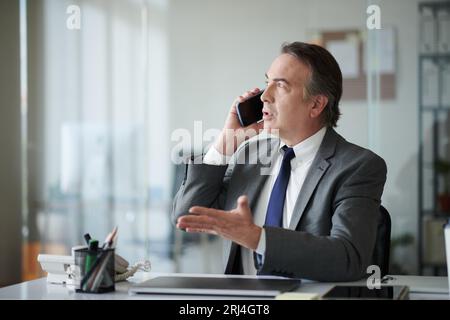 Imprenditore emotivo maturo che parla al telefono con un collega Foto Stock