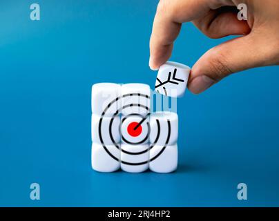 Creazione di obiettivi aziendali di successo. Ultimo blocco bianco che tiene a mano mettendo l'icona del bersaglio sul puzzle del blocco bianco su sfondo blu. Responsabile dei processi aziendali Foto Stock