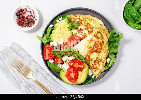 Omelette servite con avocado e pomodori ciliegini, colazione salutare su sfondo luminoso Foto Stock