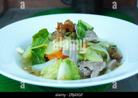 Mescolare il manzo fritto con bok choy e lattuga romaina, servito su un piatto bianco sul tavolo rivestito con foglia di banana. Foto Stock