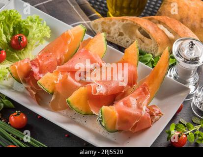 Un piatto bianco con prosciutto con fette di melone cantaloupe. Foto Stock