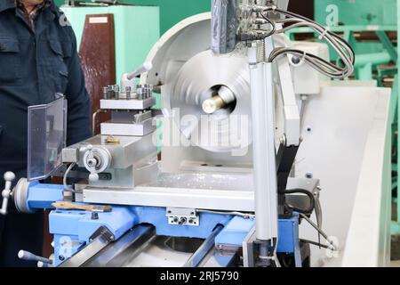 Un lavoratore maschio lavora su un più grande fabbro di ferro tornio, attrezzature per riparazioni, lavori di metallo in un'officina in un impianto metallurgico in un produ di riparazione Foto Stock