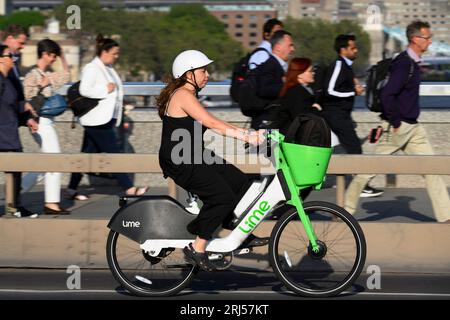 Una donna che viaggia su una bici elettrica Lime a noleggio attraverso il London Bridge durante l'ora di punta serale. London Bridge, Londra, Regno Unito. 7 giugno 2023 Foto Stock