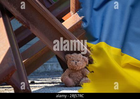 Un orsacchiotto si trova accanto a un riccio anticarro sullo sfondo della bandiera dell'Ucraina, la guerra in Ucraina Foto Stock