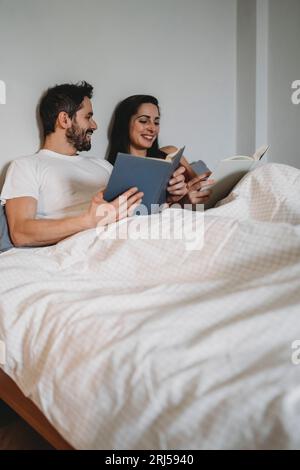 Adorabile coppia che legge sotto le coperte nel letto a casa in un momento di riposo Foto Stock