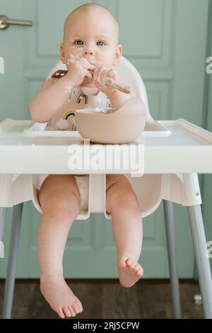 Carino bambino di sei mesi che mangia yogurt da solo Foto Stock