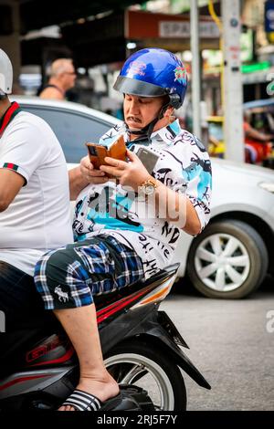 Un uomo occidentale controlla il suo cellulare mentre corre lungo Soi Buakhao, Pattaya, Thailandia, sul retro di un taxi bike. Foto Stock