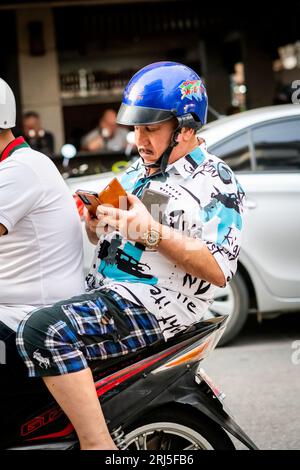 Un uomo occidentale controlla il suo cellulare mentre corre lungo Soi Buakhao, Pattaya, Thailandia, sul retro di un taxi bike. Foto Stock