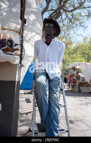 Ritratto di un uomo nero seduto su una scala, indossa un cappello e occhiali da sole, è un venditore ambulante nel mercato delle pulci Foto Stock