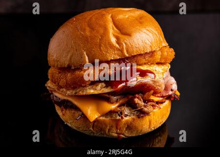 Un appetitoso hamburger di pollo con pancetta e formaggio fuso su una superficie nera Foto Stock