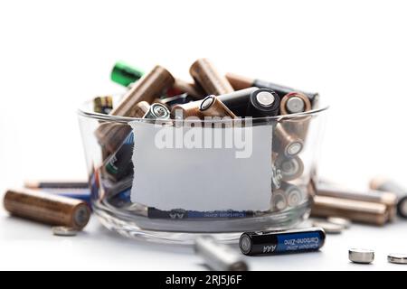 Una superficie bianca con una ciotola riempita con una varietà di batterie, che fornisce un'immagine ideale per un concetto legato all'immagazzinamento di energia e alla sostenibilità Foto Stock