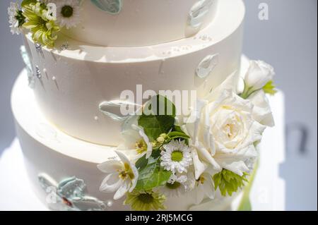 Una torta nuziale bianca a tre piani decorata con fiori bianchi Foto Stock