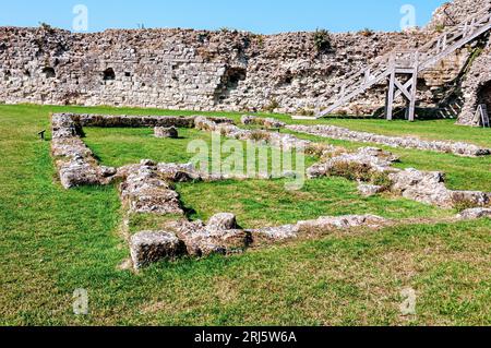 Le fondamenta in pietra della cappella del castello di Pevensey delimitano la navata nord, la piazza del coro e i resti del fonte nella navata Foto Stock