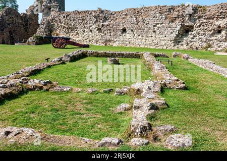 Le fondamenta in pietra della cappella del castello di Pevensey delimitano la navata nord, la piazza del coro e i resti del fonte nella navata Foto Stock