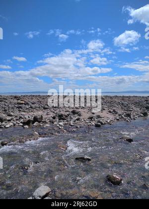 Un ruscello tranquillo si snoda attraverso un aspro terreno roccioso, incorniciato da un sereno sfondo di un cielo azzurro Foto Stock