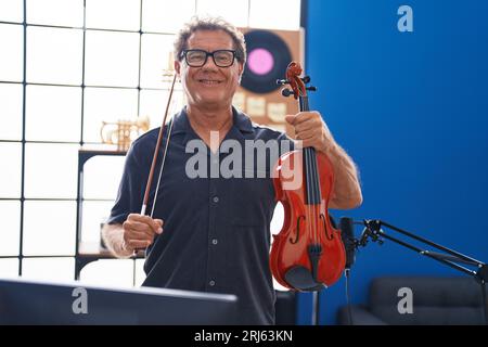 L'uomo di media età musicista sorridente sicuro tenendo il violino allo studio di musica Foto Stock