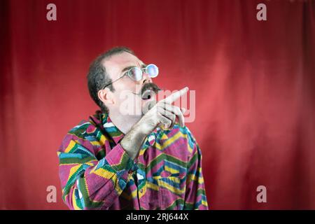 Uomo hipster con occhiali e baffi stupiti mentre punta il dito verso l'alto Foto Stock