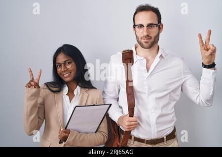 Coppia interrazziale che indossa occhiali sorridenti guardando la telecamera che mostra le dita che fanno il segno della vittoria. numero due. Foto Stock