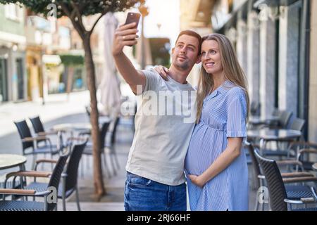 Coppia uomo e donna che si aspettano il bambino fare selfie da smartphone alla terrazza del bar Foto Stock