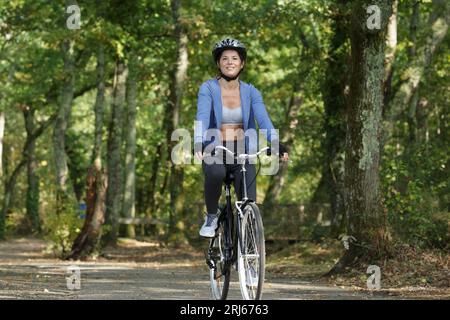 bella donna che pedala lungo un sentiero alberato Foto Stock