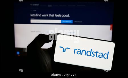 Persona che possiede un telefono cellulare con il logo della società olandese delle risorse umane Randstad NV sullo schermo davanti alla pagina Web. Concentrarsi sul display del telefono. Foto Stock