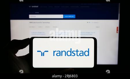 Persona in possesso di un cellulare con il logo della società olandese delle risorse umane Randstad N.V. sullo schermo di fronte alla pagina Web aziendale. Concentrarsi sul display del telefono. Foto Stock