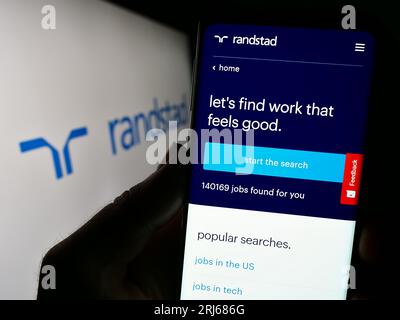 Smartphone con pagina Web dell'azienda olandese di risorse umane Randstad N.V. sullo schermo davanti al logo aziendale. Concentrarsi sul centro del display del telefono. Foto Stock