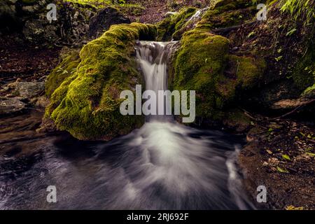 Una cascata panoramica scende lungo il fianco di una montagna rocciosa e muscolosa Foto Stock