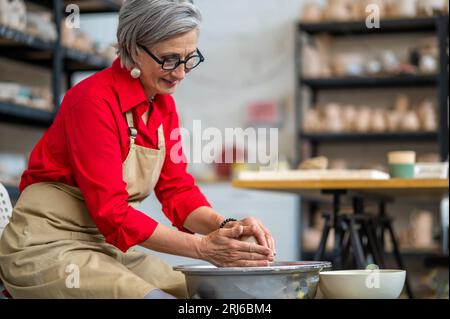 Donna che lavora alla ruota dei ceramisti che crea prodotti in argilla presso la sua officina. Foto Stock